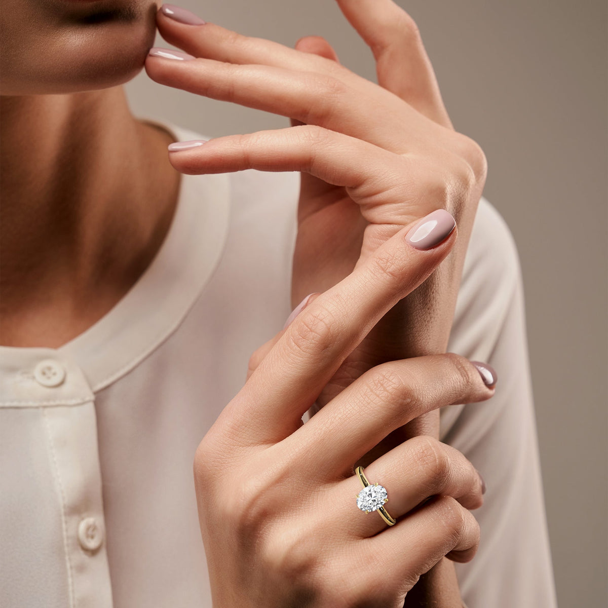 Close-up of a woman's hand wearing a gold ring with a diamond on a neutral background 